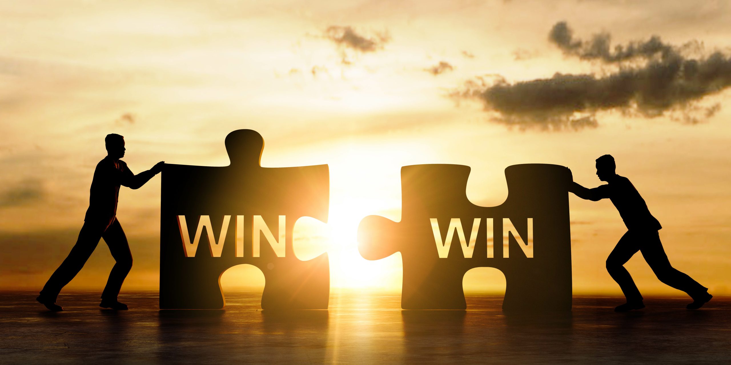 Against a golden sunset sky, two silhouetted figures push matching puzzle pieces toward the center. Each puzzle piece displays the word “WIN,” and the pieces are positioned to connect, representing teamwork, mutual success, collaboration, and shared goals.
